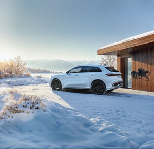 Q5 e-hybrid sedd från sidan. Står parkerad bredvid ett trähus i vinterlandskap med berg i bakgrunden.